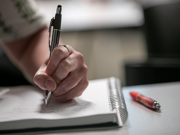 A hand holds a pen to a notebook.